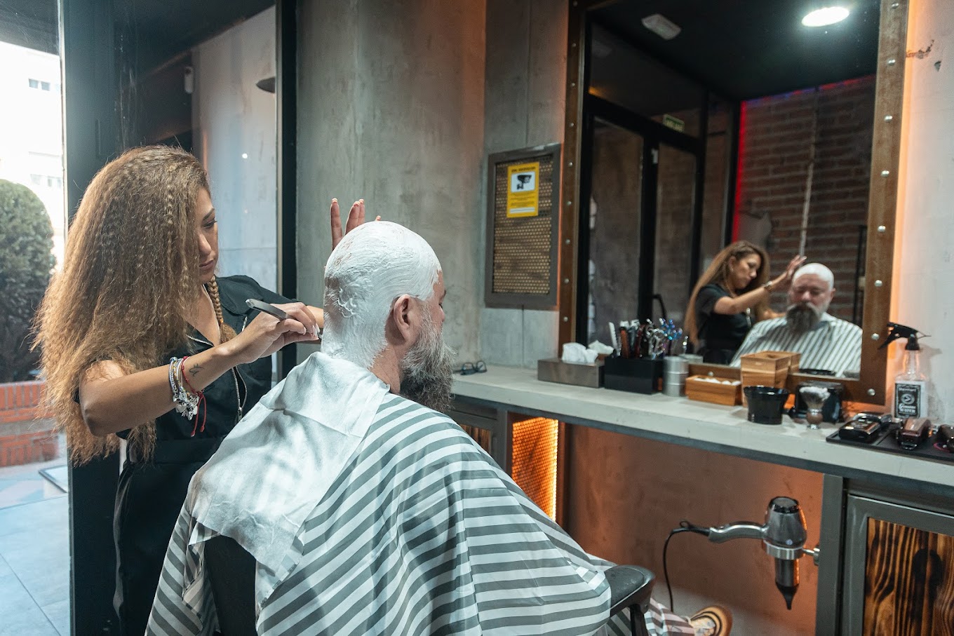 Barbera trabajando en el corte de cabello de un cliente con barba en The Original Barber Shop.