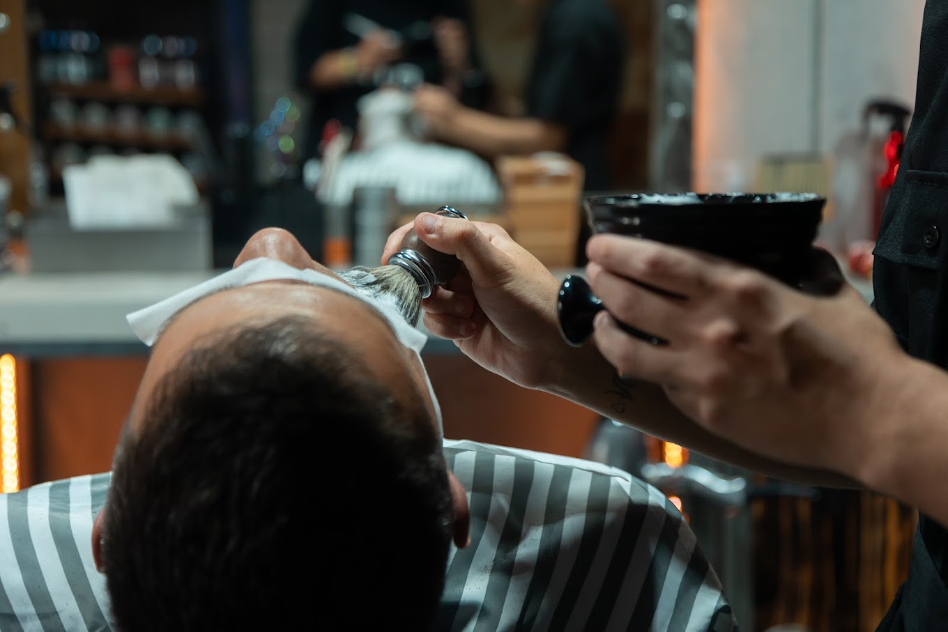 Barbero preparando espuma para afeitar a un cliente en The Original Barber Shop.